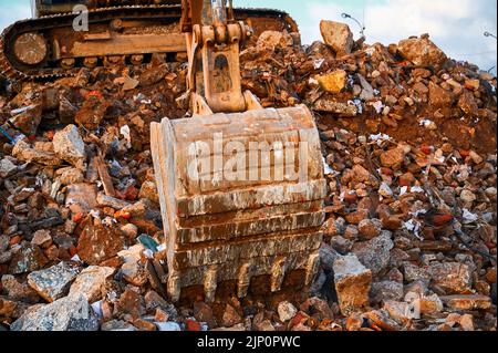 Der Eimer eines Baubaggers schaufelt zerstörten Beton und Ziegel sowie große Stapel auf. Stockfoto