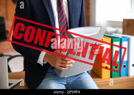 Junger Mann hält Ordner mit streng geheimen Dokumenten im Büro Stockfoto