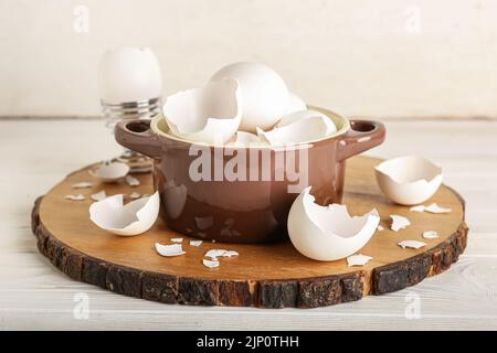 Brett mit zerbrochenen Eierschalen im Kochtopf auf weißem Holzhintergrund Stockfoto