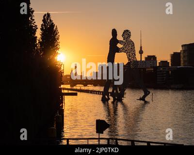 Sonnenuntergang auf der Spree in Berlin. Die Skulptur Molecule man von Jonathan Borofsky befindet sich vor der Skyline der Stadt mit dem Fernsehturm. Stockfoto