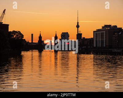 Skyline der Stadt in Berlin. Gebäude wie der Fernsehturm und die Oberbaumbrücke sind in Silhouette. Die Sonne geht unter und färbt den Himmel. Stockfoto