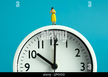 Miniatur Menschen Spielzeug Figur Fotografie. Ableseroutine Konzept. Eine Studentin stand und las ein Buch über der Uhr. Bildfoto Stockfoto