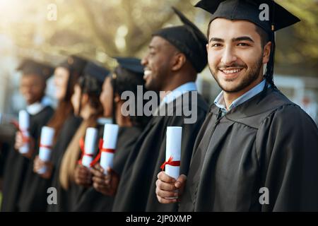 Stolz beginnt nicht, das Gefühl zu beschreiben. Porträt eines jungen Mannes, der sein Diplom hält, während er mit seinen Mitstudenten am Abschlusstag steht. Stockfoto