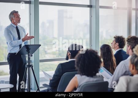 HES hat eine Fülle von Erfahrungen zu teilen. Eine Aufnahme eines hübschen, reifen Sprechers, der sich während eines Seminars in an eine Gruppe von Geschäftsleuten wendet Stockfoto