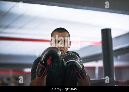 Arbeiten an seiner Technik. Beschnittenes Porträt eines jungen männlichen Athleten, der in einem Boxring trainiert. Stockfoto