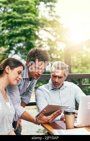 Das wird die Revolution sein: Ein Team von Kollegen, die bei einem Treffen im Freien zusammen einen Laptop und ein digitales Tablet nutzen. Stockfoto