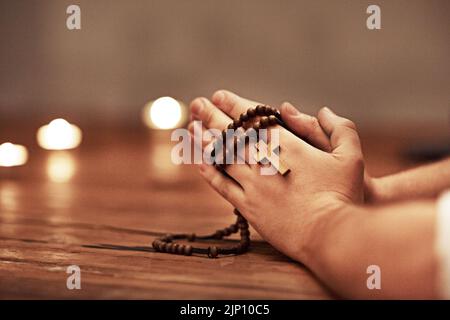 Person Hände beten mit einem Rosenkranz mit Kreuz des christlichen Glaubens, Religion oder Tradition in einer religiösen Kirche Nahaufnahme und Hintergrund. Mann Katholisch Stockfoto