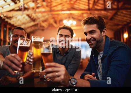 Erinnerungen auf die beste Art und Weise zu machen, die wir kennen: Eine Gruppe junger Freunde saß zusammen an einem Tisch, während sie ein Bier genossen und mit einem Festakt feierten Stockfoto