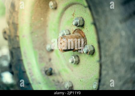 Die Achse des Rades eines begehbaren Traktors ist mit Rost aus der Nähe bedeckt. Das Rad eines grünen Traktors montieren Stockfoto