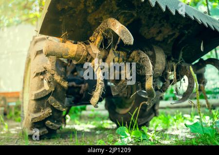 Aktiver Motoblock-Schneider im Schlamm aus der Nähe, Ansicht von unten. Kleiner Traktor zum Pflügen eines Gemüsegartens in der Landwirtschaft Stockfoto