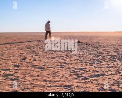 Botswana Afrika - August 29 2007; Mann, der durch die Wüste läuft und Staub im Sand unter blauem Himmel aufsautiert Stockfoto