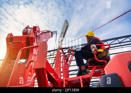 Asian Crane Driver, Crane Driver sitzt ein Top in einer mobilen Krankabine und arbeitet beim Heben des Dachs oder PU-Schaum-Dachblech auf der Baustelle. Stockfoto