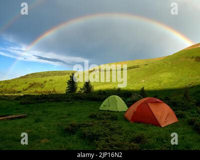 Ein Touristenzelt in den Bergen auf dem Hintergrund eines Regenbogens. Stockfoto