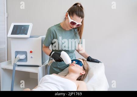 Therapeut Kosmetologe durchläuft Laser-Behandlung auf Gesicht junge Frau in Beauty-Klinik. Gesichtslaserhaar. Epilierverfahren. Zufriedener Kunde, selektiver Fokus. Stockfoto