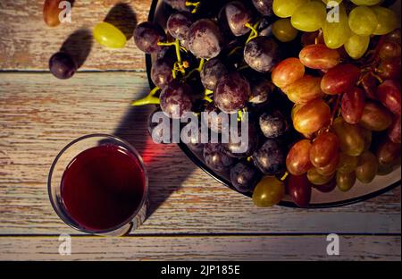 Ein Teller mit Trauben aus schwarzen, weißen und rosa Trauben und einem Glas Rotwein Stockfoto