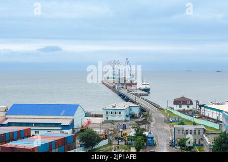 Korsakov, Russland - 04. August 2022: Frachtliegeplatz mit Hafenkranen und festgetäuten Schiffen vor dem Hintergrund des offenen Meeres Stockfoto