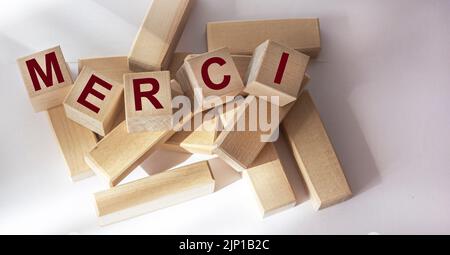 Merci - Danke auf Französisch. Das Wort Merci auf Holzwürfeln auf weißem Hintergrund. Stockfoto