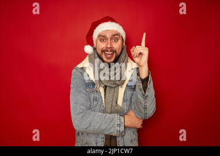 Aufgeregt lächelnden Mann in Weihnachtshut hält Zeigefinger hoch freut gute Idee des Geschenks für das neue Jahr Stockfoto