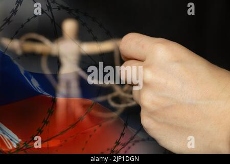 Die Hand zieht die Seile an der Puppe vor dem Hintergrund der russischen Flagge und Stacheldraht, russische Sklavin und Propagandist in Russland, stoppen t Stockfoto