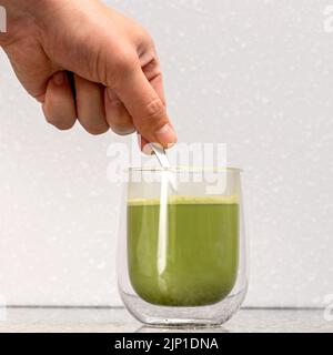 Grüner Matcha-Latte-Tee in einem Glas. Grüner Matcha Latte wird in ein transparentes Glas mit doppeltem Boden gegossen Stockfoto