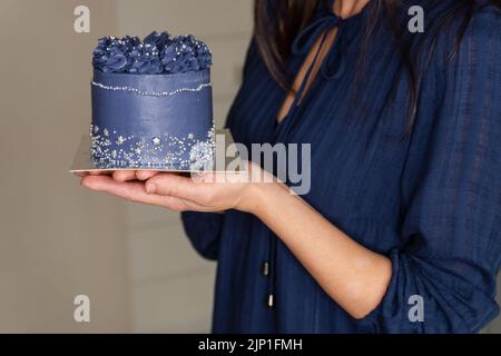 Der Konditor hält einen kleinen Kuchen. Lächelnde junge Frau mit Cupcake Stockfoto