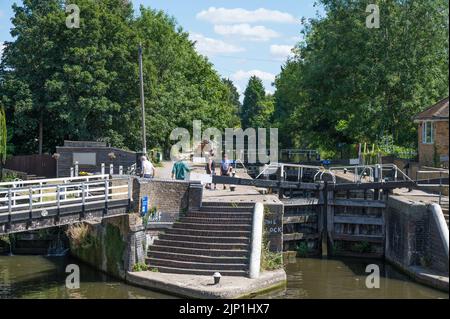 Junge Frau und zwei Jungen beobachten, wie ein Mann das Schleusentor für ein kleines Boot schließt, das durch Batchworth Lock, Rickmansworth, Hertfordshire, England, Großbritannien, fährt. Stockfoto