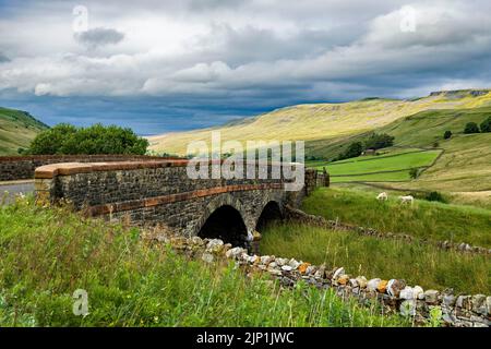 Eine freie Sicht auf Mallerstang Edge mit der Sonne, die den oberen Bereich aussticht. Die Brücke im Vordergrund überquert die Carlisle, um die Eisenbahn anzusiedeln. Stockfoto