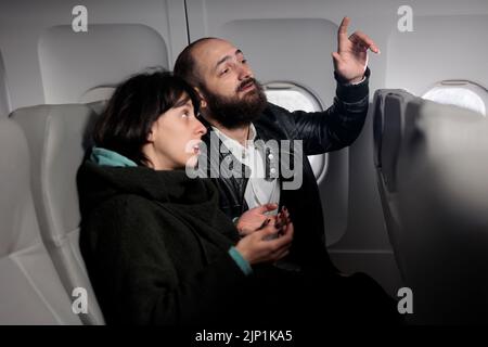 Ein paar Touristen, die auf den Flug warten und in der Economy Class sitzen, warten auf den Abflug. Mann bat den Flugbegleiter um Hilfe und flog mit einem internationalen Flugzeug, um im Urlaub zu reisen. Stockfoto