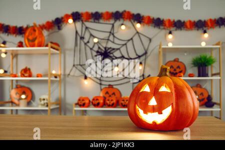Kürbis mit geschnitztem lustig glühendem Gesicht, das auf dem Hintergrund von Halloween Dekor steht. Stockfoto