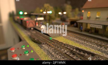 Modell Dampflokomotive durch Station. Mini-Personenzug bewegt sich auf Mini-Eisenbahn. Stockfoto