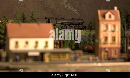 Landschaftlich schöner Spielzeugzug der Bergbahn. Spielzeuglokomotive, die sich auf einer Brücke bewegt. Eisenbahnverkehrskonzept. Stockfoto