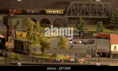 Modellzug bewegt sich auf der Brücke. Elektrische Lokomotive auf den Gleisen. Stadt in Miniatur. Modelleisenbahnausstellung. Stockfoto