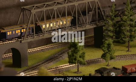 Modell vintage Zug durch Brücke bewegen. Blaue elektrische Lokomotive auf Schienen. Dampf- und Dieselzüge auf der Modellbahn. Stockfoto