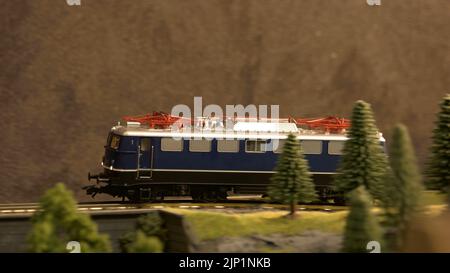 Modell der Eisenbahndiesellokomotive, die auf der Eisenbahn fährt. Miniaturzug, der durch den Wald in den Bergen fährt. Stockfoto