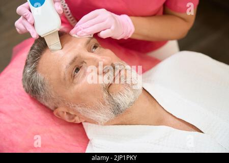 Frau Hand Kosmetikerin macht männliche Verfahren der Ultraschallreinigung Gesicht Stockfoto