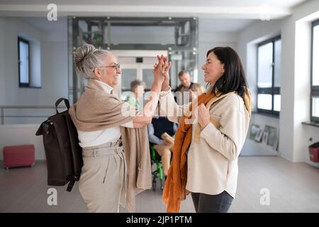 Glückliche ältere Studentinnen treffen sich im Korridor an der Universität mit hohen Fünffälern. Stockfoto