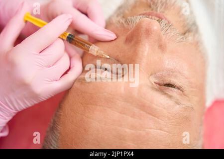Kosmetikerin Hände machen Beauty-Injektion an den Mann unter Augen Stockfoto