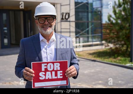Lächelnder Vorarbeiter hält Schild mit Aufschrift zum Verkauf Stockfoto