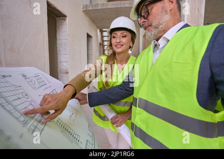 Vorarbeiter hält erweiterte Zeichnung, und realtor zeigt auf sie Hand Stockfoto