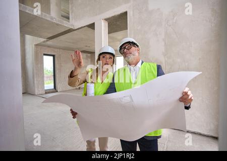 Der Vorarbeiter hält einen Plan und bespricht ihn mit dem Immobilienmanager Stockfoto