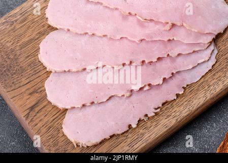 Geschnittener Schinken auf Holzschneidebrett. Schwarzer Betonhintergrund Stockfoto