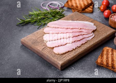 Geschnittener Schinken auf Holzschneidebrett. Schwarzer Betonhintergrund Stockfoto