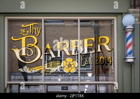 Thy Barber, Barber Schaufenster mit reich verzierten goldfarbenen Fensterschild und Barber Stange Spitalfields London UK Stockfoto