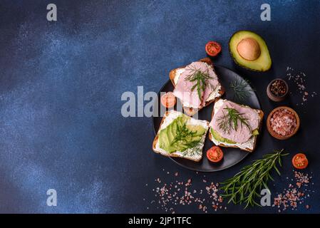 Frische, leckere Sandwiches mit Schinken, Butter, Avocado und Sesam auf einem Holzbrett. Leckere gesunde Lebensmittel Stockfoto