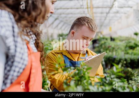 Erfahrene Frau Floristin hilft jungen Angestellten mit Down-Syndrom im Gartencenter. Stockfoto