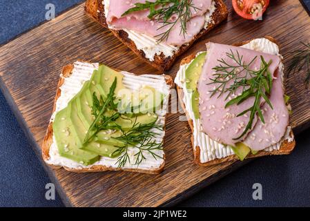 Frische, leckere Sandwiches mit Schinken, Butter, Avocado und Sesam auf einem Holzbrett. Leckere gesunde Lebensmittel Stockfoto