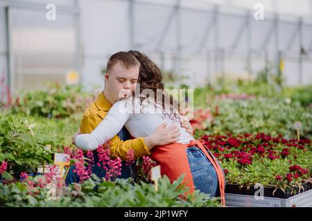 Frau Floristin umarmt ihren jungen Kollegen mit Down-Syndrom in Gartencenter. Stockfoto