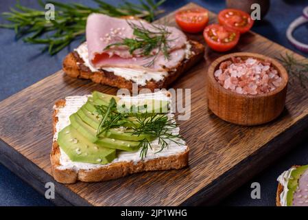 Frische, leckere Sandwiches mit Schinken, Butter, Avocado und Sesam auf einem Holzbrett. Leckere gesunde Lebensmittel Stockfoto