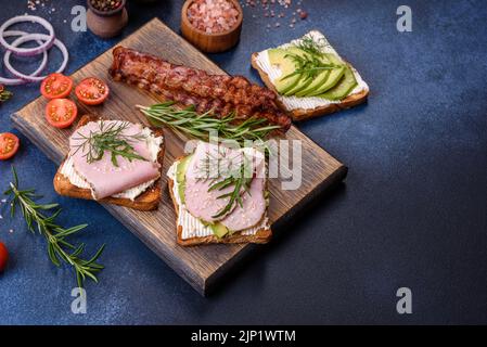 Frische, leckere Sandwiches mit Schinken, Butter, Avocado und Sesam auf einem Holzbrett. Leckere gesunde Lebensmittel Stockfoto