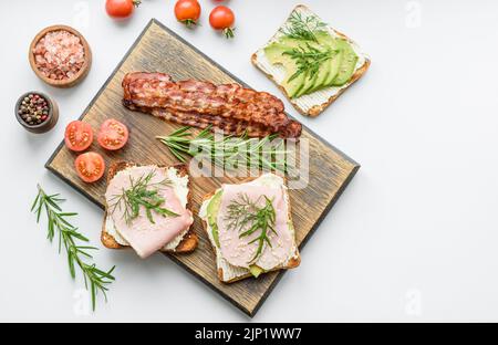 Frische, leckere Sandwiches mit Schinken, Butter, Avocado und Sesam auf einem Holzbrett. Leckere gesunde Lebensmittel Stockfoto